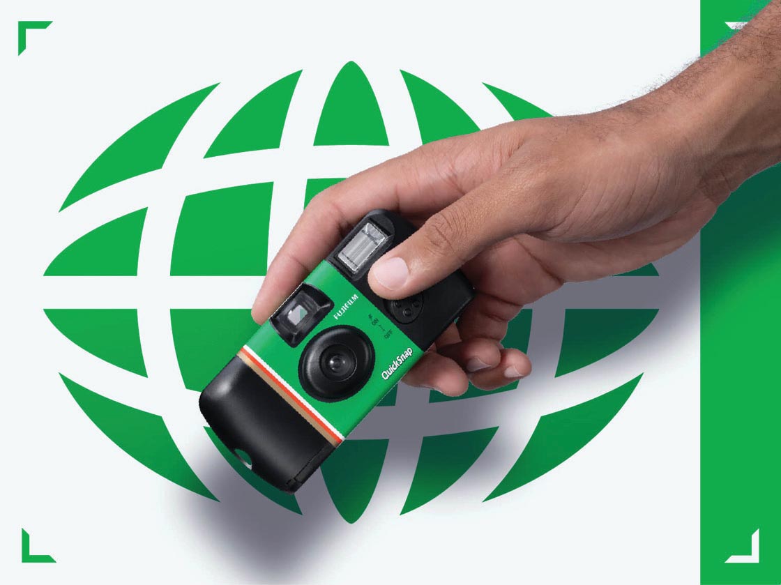 A hand holding a FUJIFILM QuickSnap camera in front of a circular globe graphic